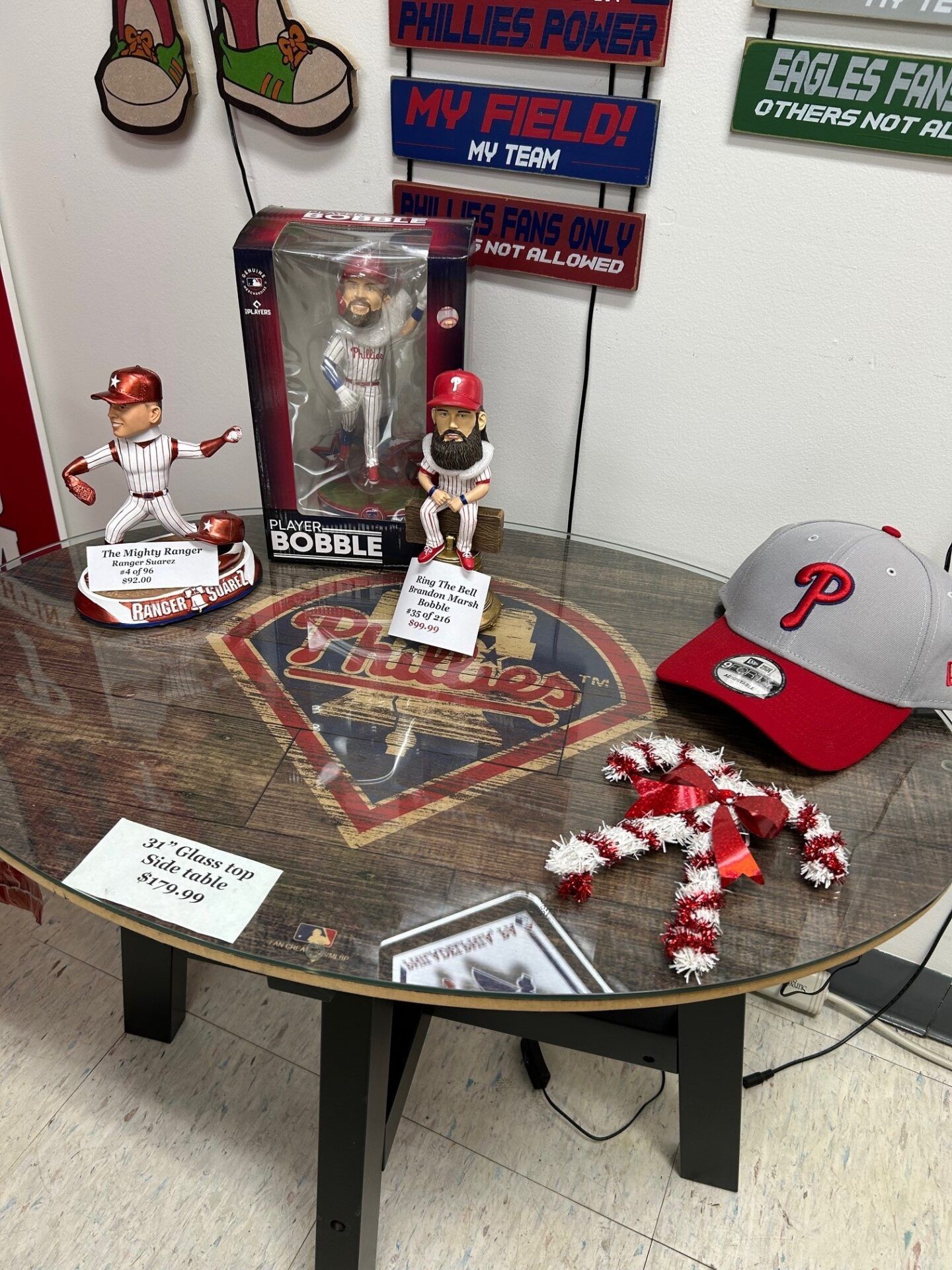 Philadelphia Phillies fan memorial table with bobbleheads, baseballs, and red hat displays on a wall-mounted shelf