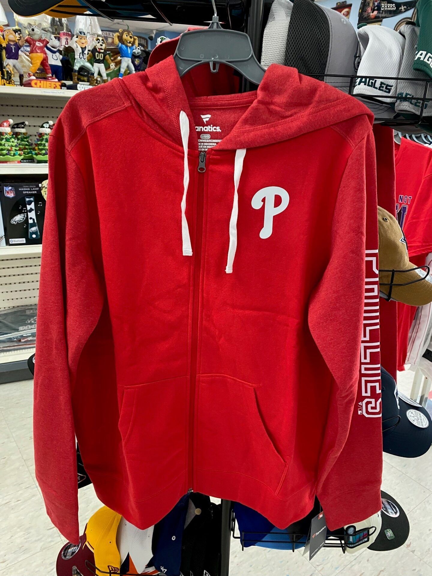 Red zip-up hoodie with white drawstrings and a white “P” logo hanging in a clothing store.