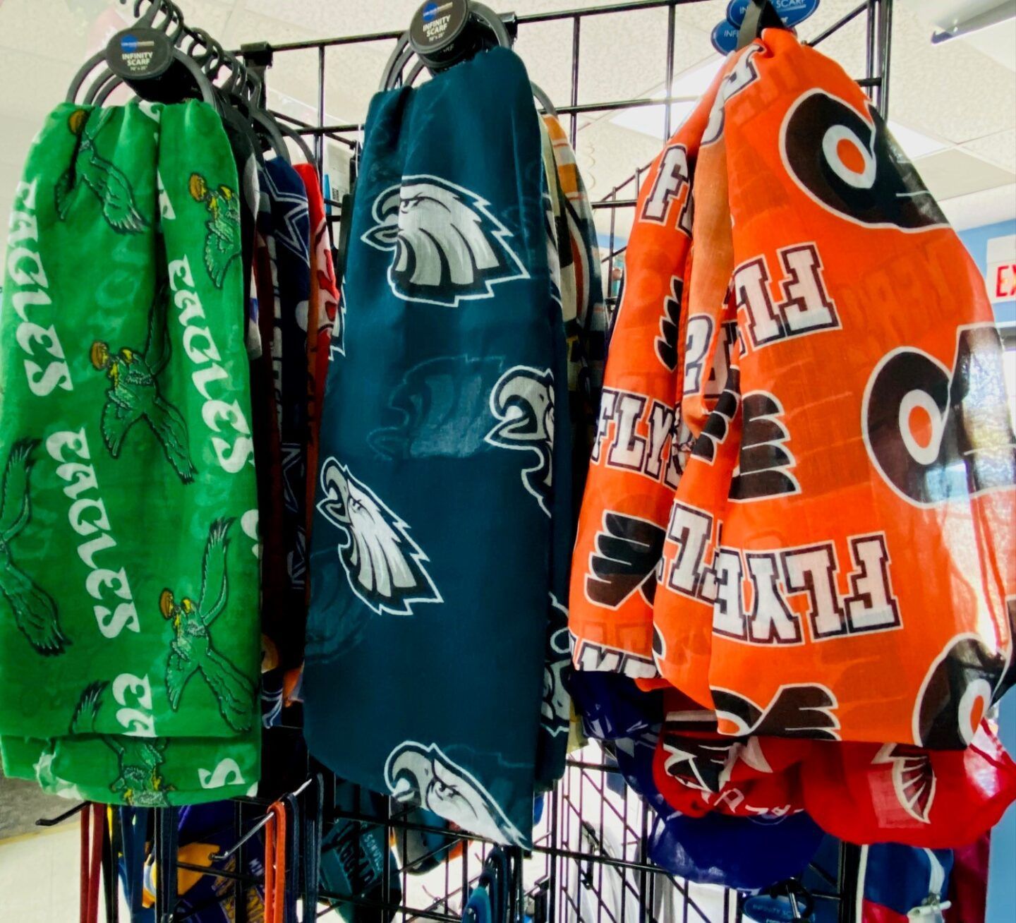 Bright team-patterned blankets or towels hanging on a wire rack in green, blue, and orange.