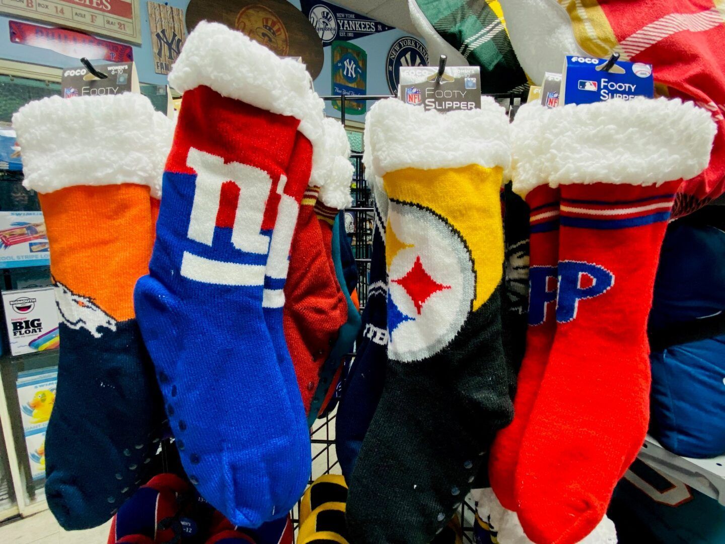 Four fuzzy holiday stockings in blue, red, orange, and black, hanging in a store display.
