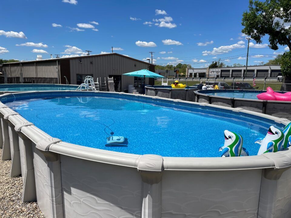 Above-ground backyard pool with blue water, white fence, and outdoor furniture under a sunny sky