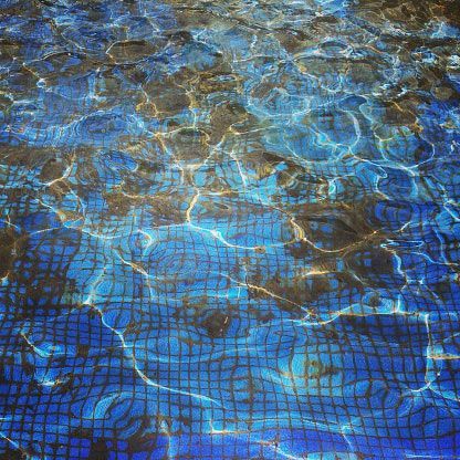 Blue swimming pool water with sunlight ripples over a dark tiled surface