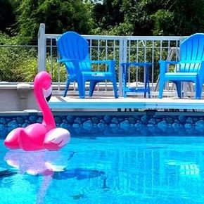 Pink flamingo float in a backyard pool with blue chairs and a white fence in the background