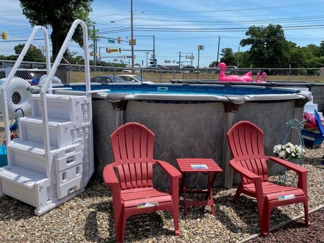Red and white chairs beside an above-ground pool with a pink flamingo float in a gravel yard