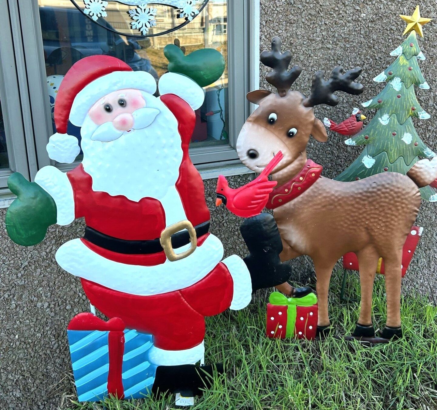 Santa and a reindeer holiday lawn display beside wrapped gifts and a decorated Christmas tree