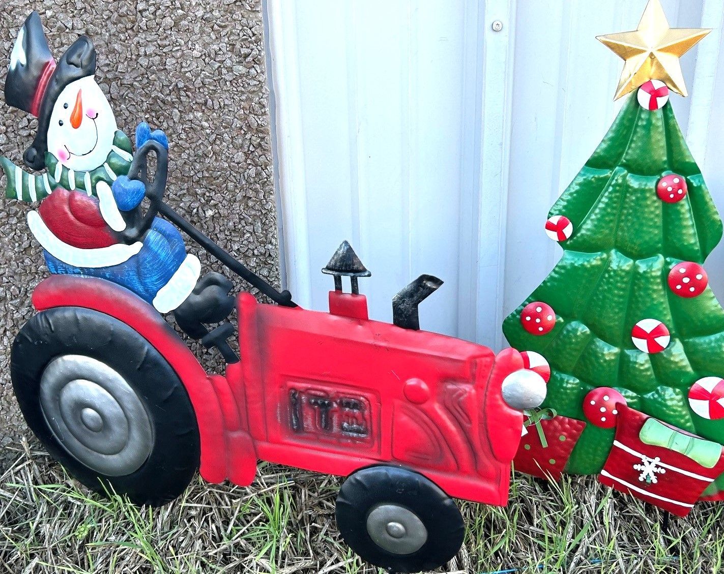 Red toy tractor with a snowman decoration and Christmas tree ornament outdoors on grass.