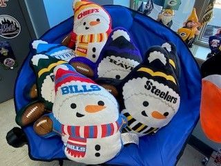 Three football-themed snowman plushes on a blue chair, including Chiefs, Bills, and Steelers.