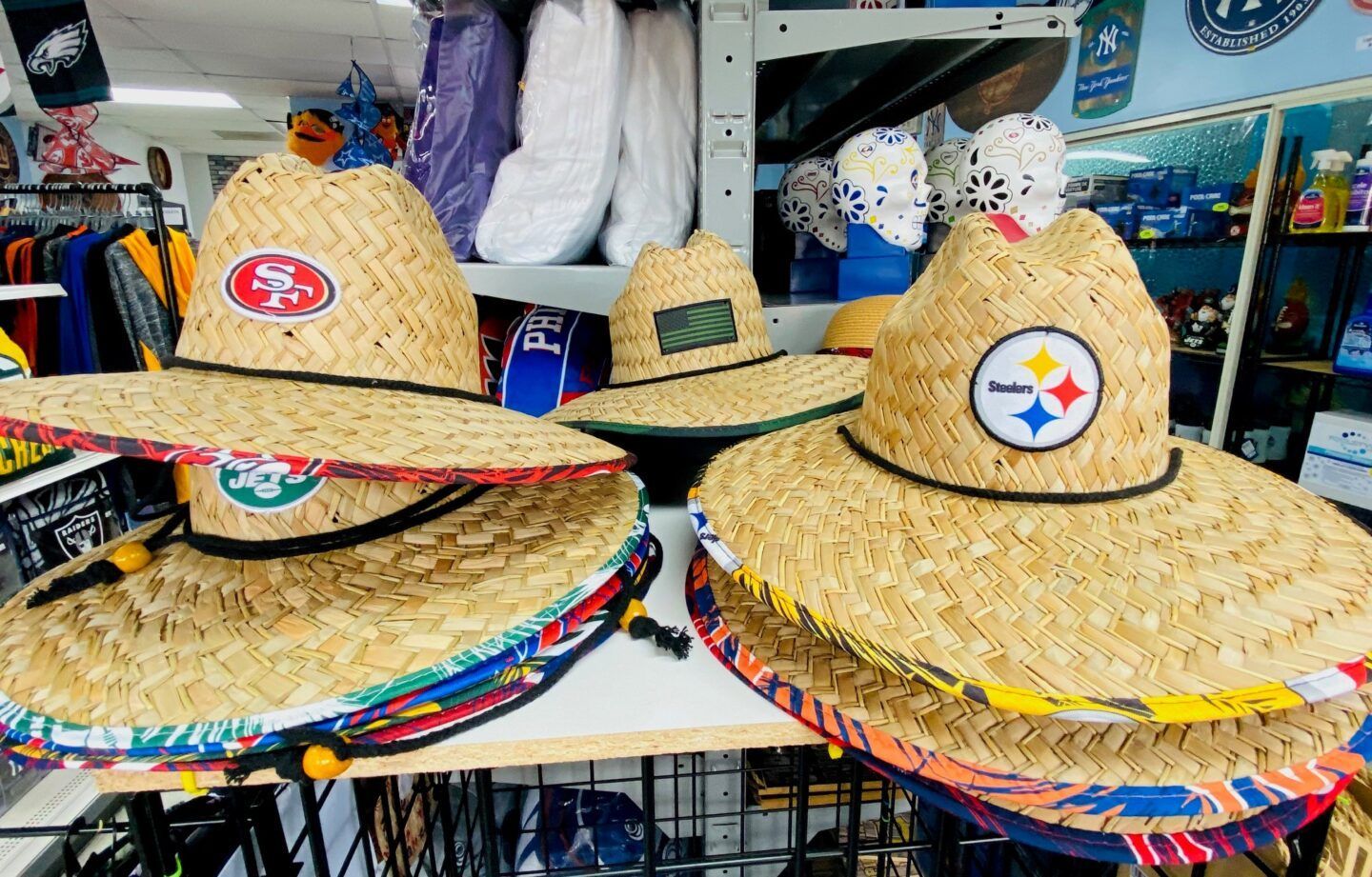 Straw hats with colorful trim and sports logos displayed on a market shelf