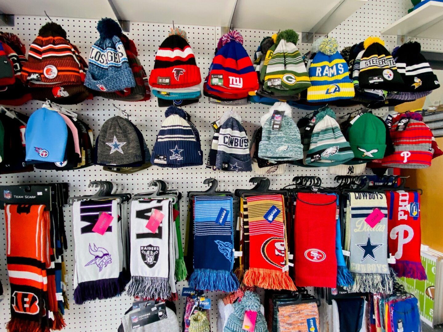 Display of colorful knit hats and scarves hanging on a pegboard wall in a shop