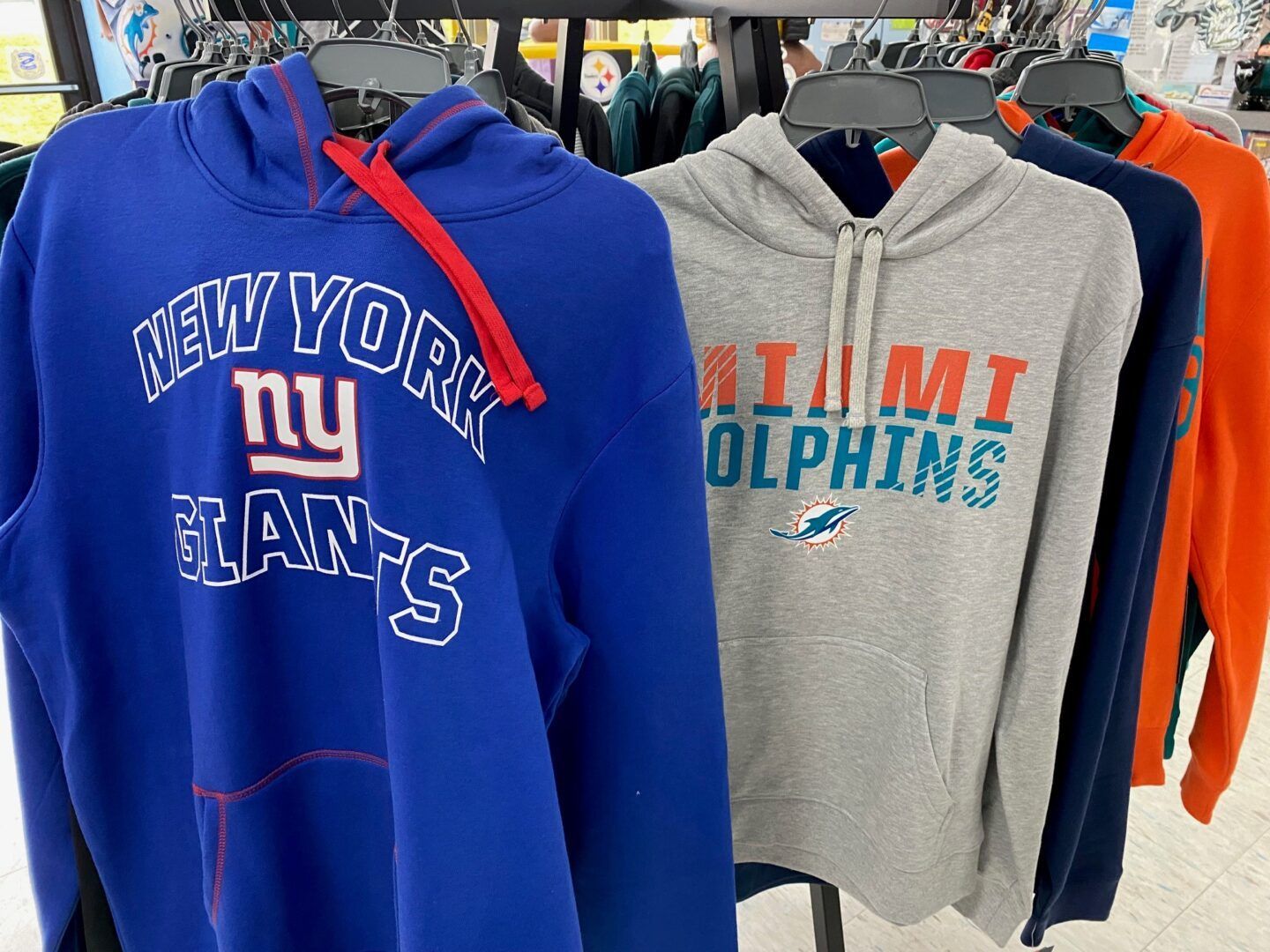 Assorted hoodies on a clothing rack, including blue New York Giants and gray Miami Dolphins sweatshirts