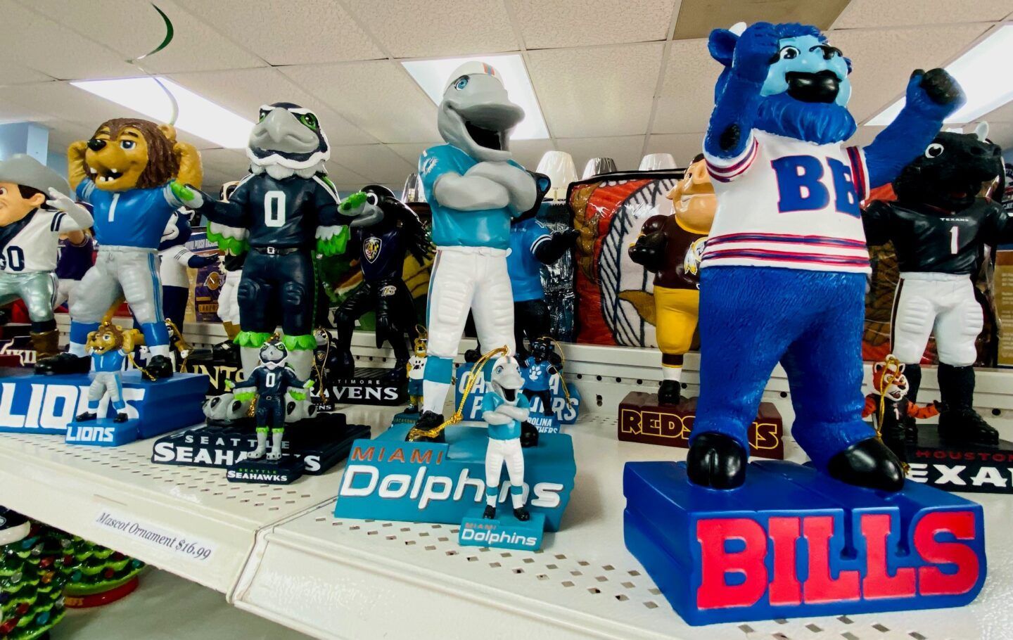 NFL team mascot bobbleheads on a store shelf, including Buffalo Bills, Dolphins, Seahawks, and Texans figures.