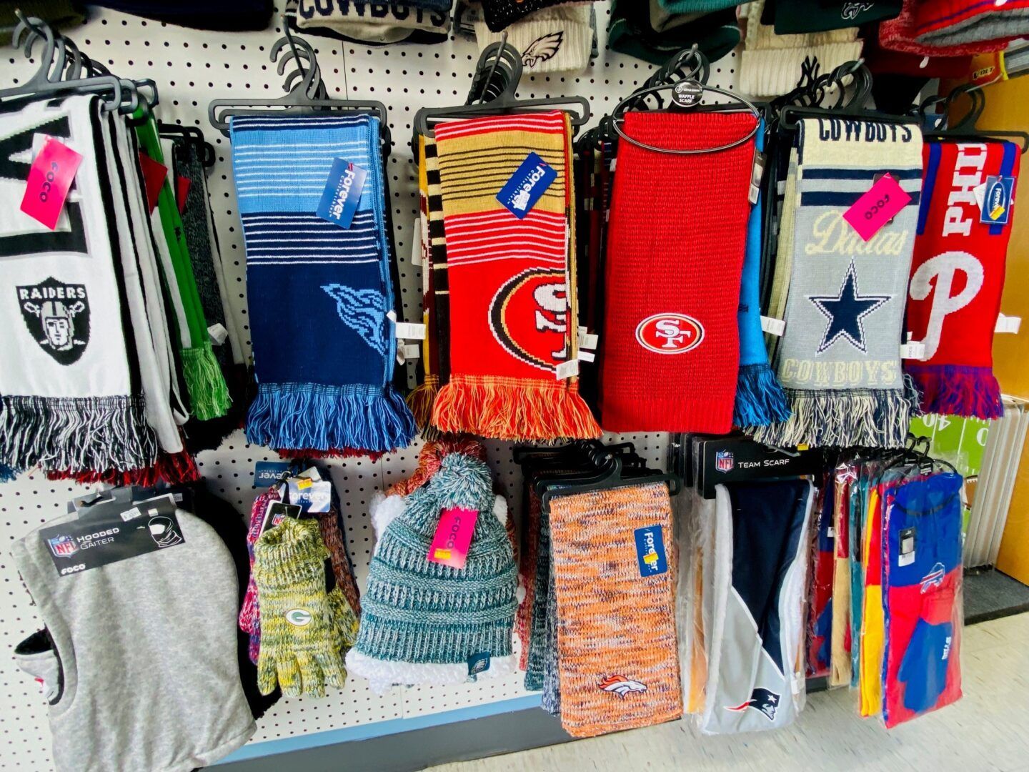 Sports team scarves and knit hats hanging in rows on a store display rack.