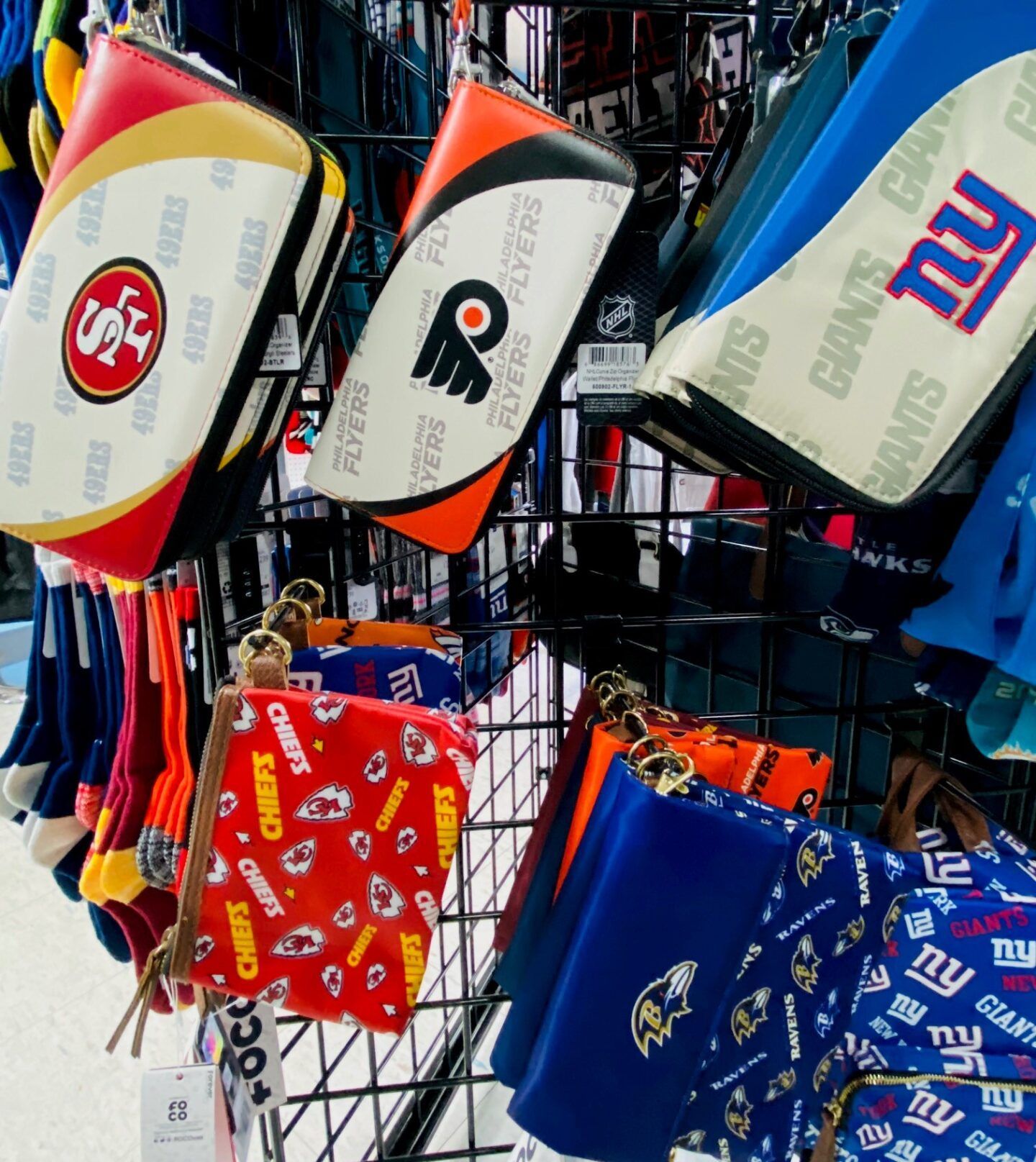 Colorful NFL team backpacks hanging in a store display, including Giants, Eagles, and 49ers designs