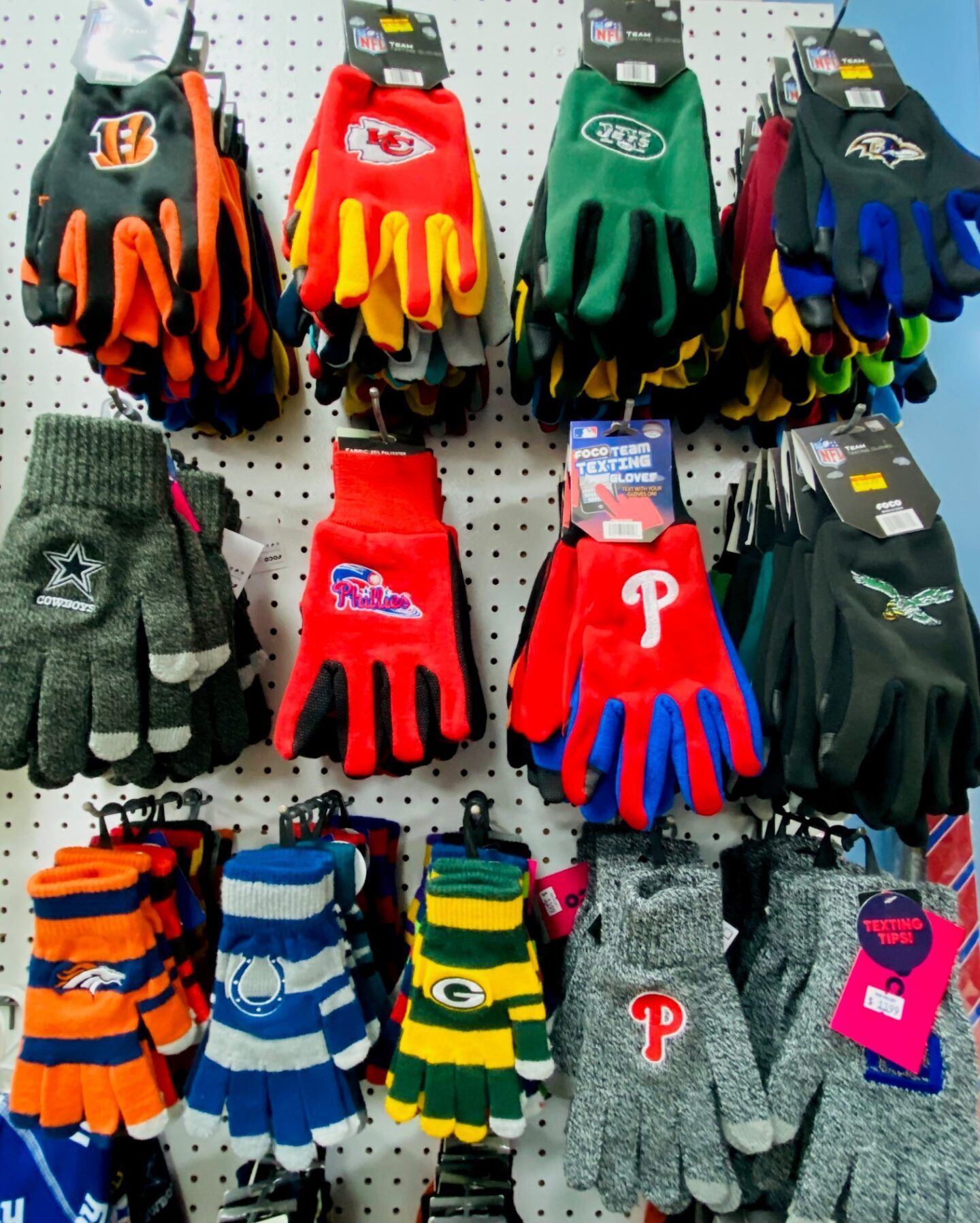 Gloves displayed on a store pegboard, in orange, red, green, blue, gray, and striped colors.