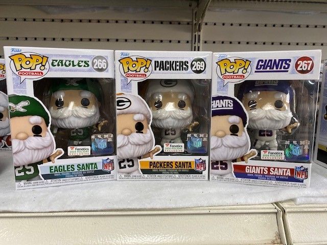 Three Funko Pop NFL Santa figures: Eagles, Packers, and Giants on a store shelf.