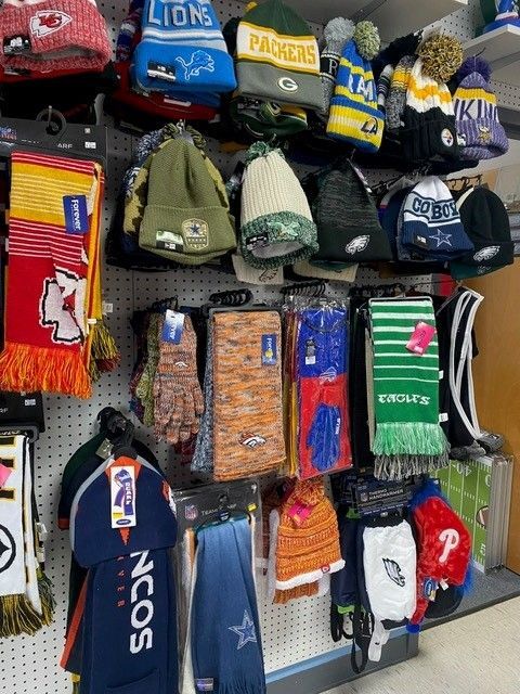 Assorted sports team scarves and hats displayed on a store rack, in bright colors and patterns