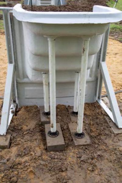 White fiberglass tank on white metal legs in muddy outdoor ground
