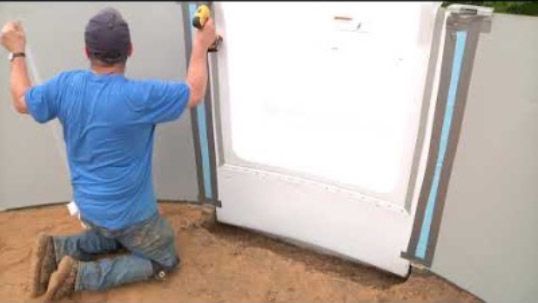 Person kneeling while installing a wall panel with blue trim using a yellow tool