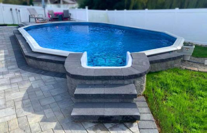 Blue in-ground pool with gray stone deck and steps in a backyard