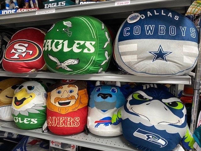 Row of NFL team-themed pillows and plush toys, including 49ers, Eagles, Cowboys, and Seahawks colors