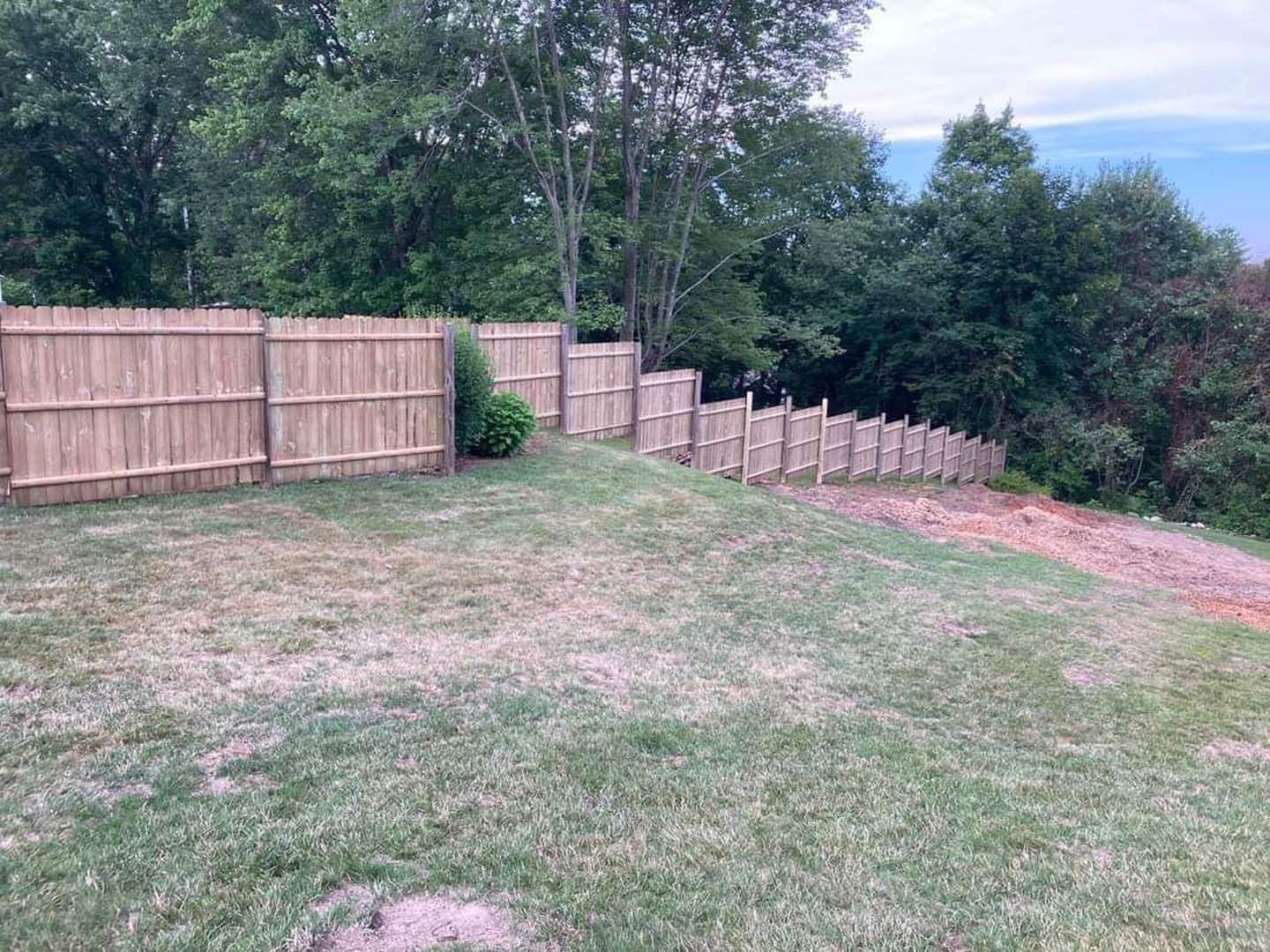 A wooden fence surrounds a grassy field with trees in the background.