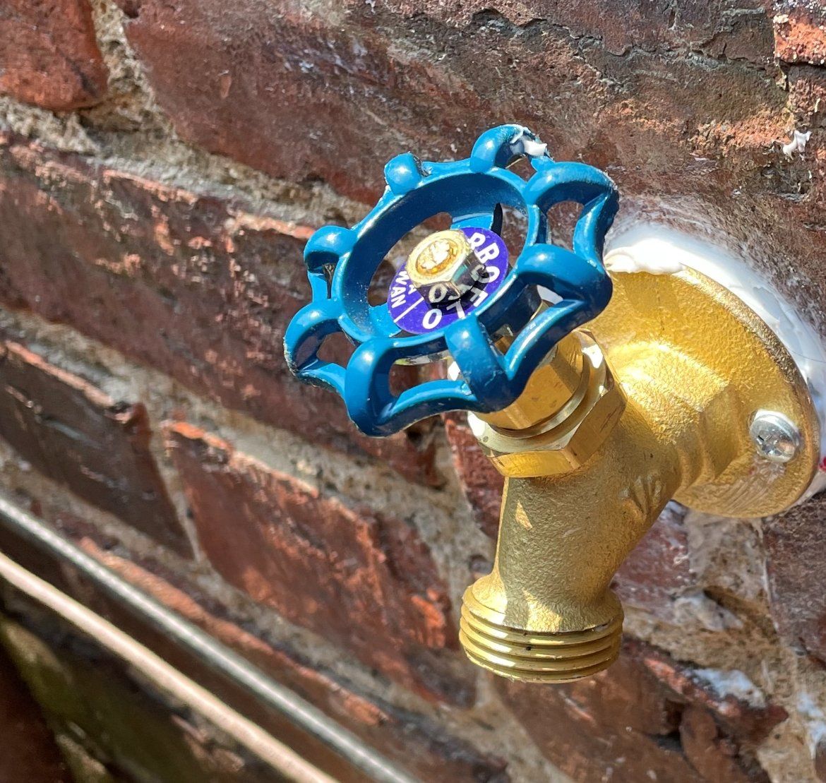 Blue handled outdoor water faucet on a brick wall.