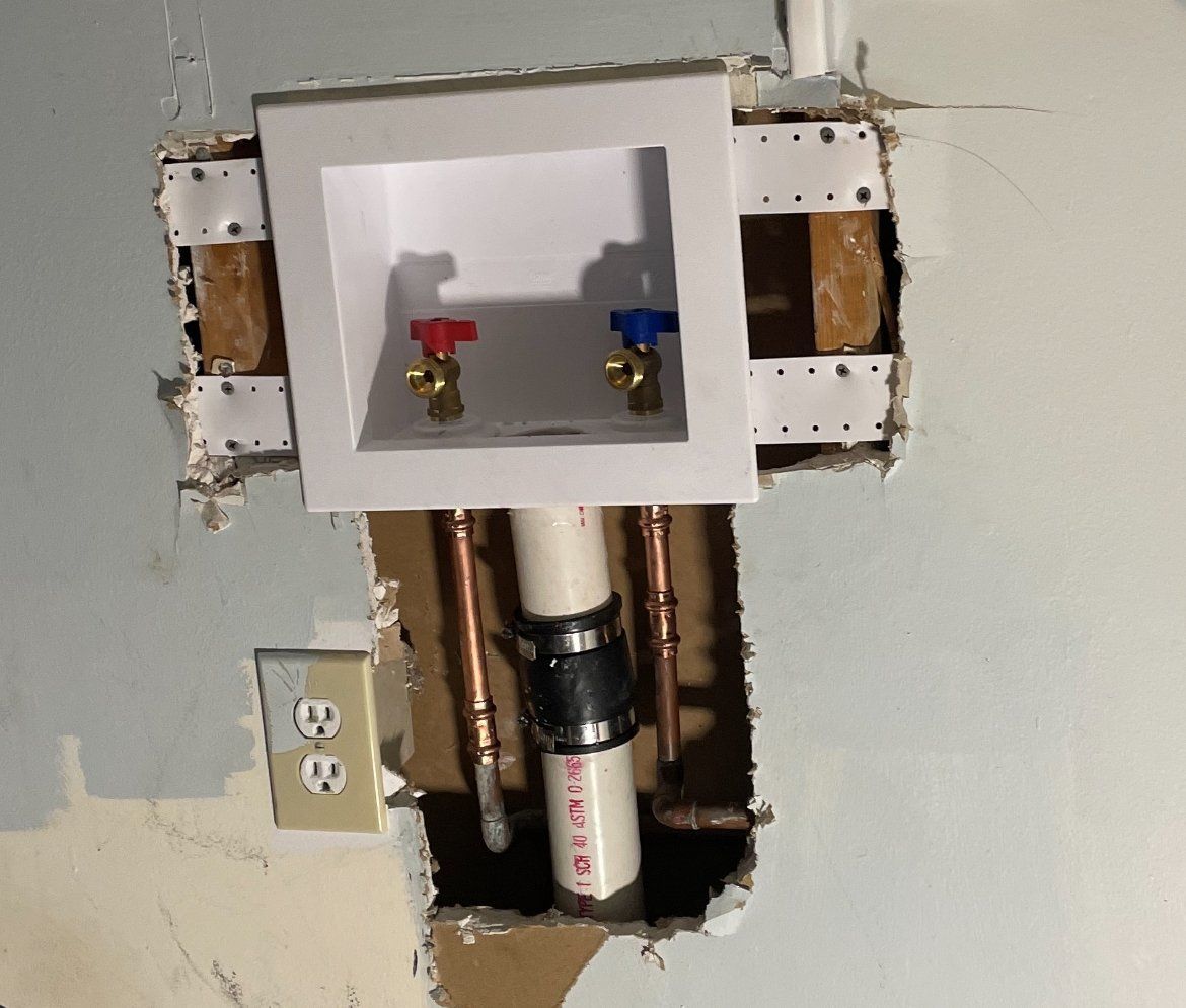 Laundry water hookup with red and blue valves in a white box, installed in a wall.