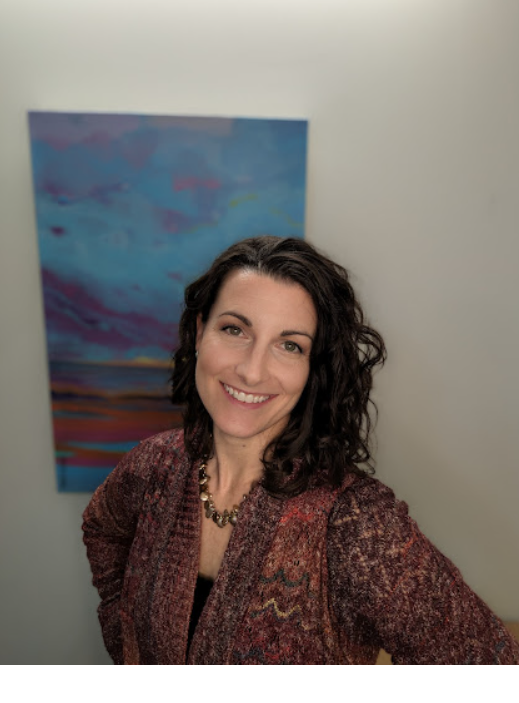 Une femme sourit devant un tableau sur un mur.
