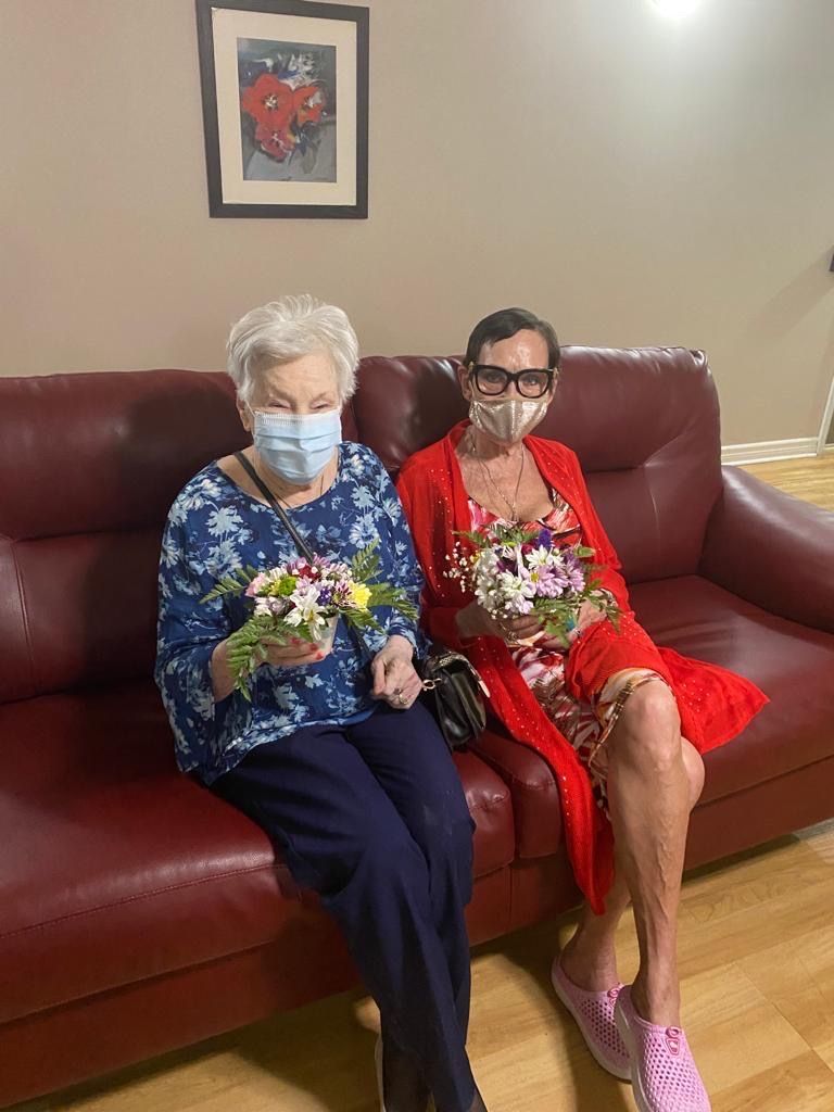 Deux femmes portant des masques faciaux sont assises sur un canapé tenant des fleurs.