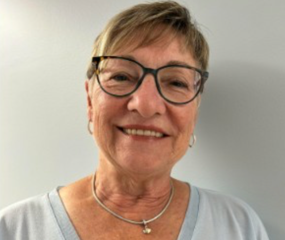 Une femme portant des lunettes et un collier sourit à la caméra