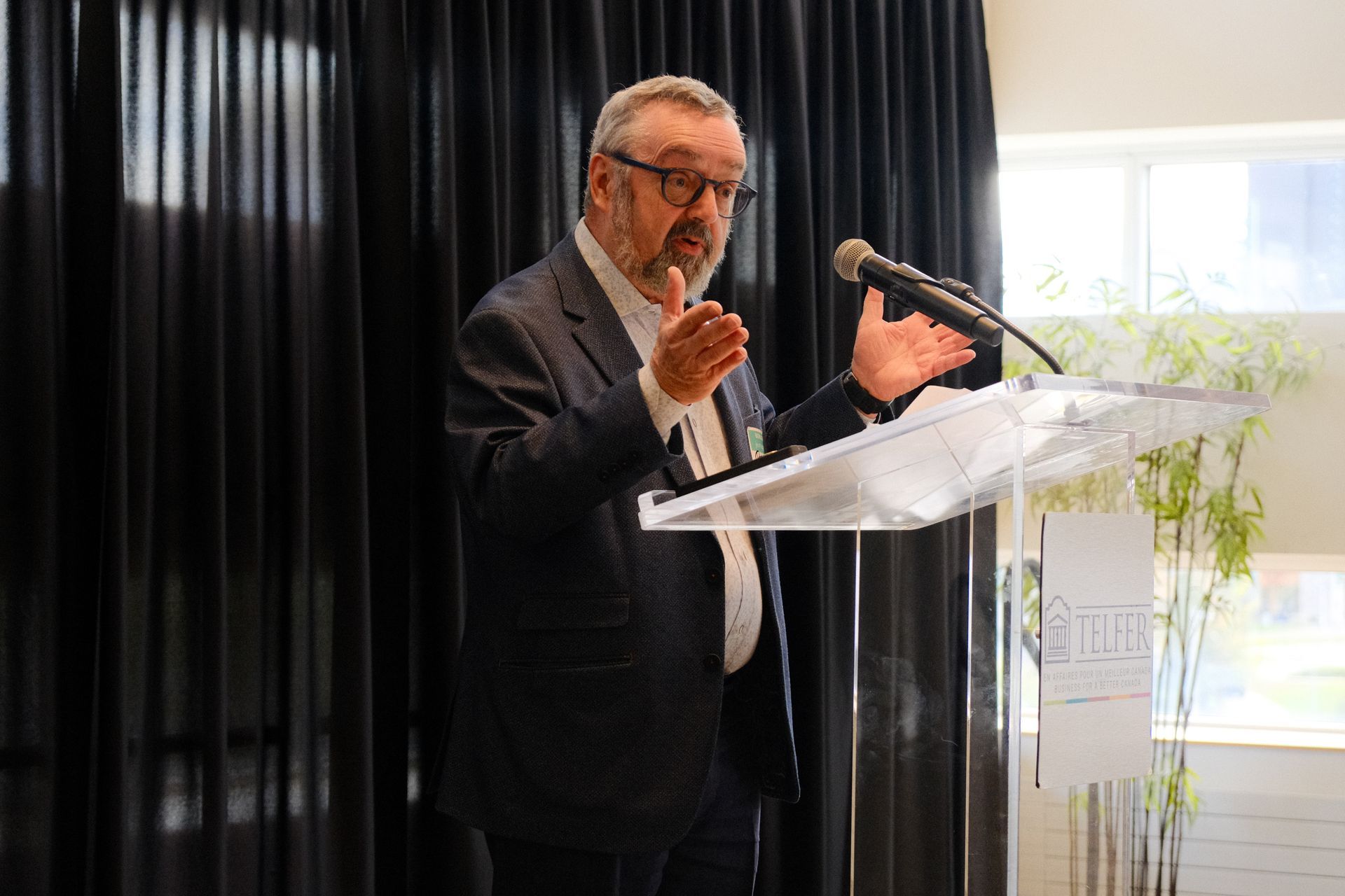Un homme en costume et lunettes se tient sur un podium et parle dans un microphone.