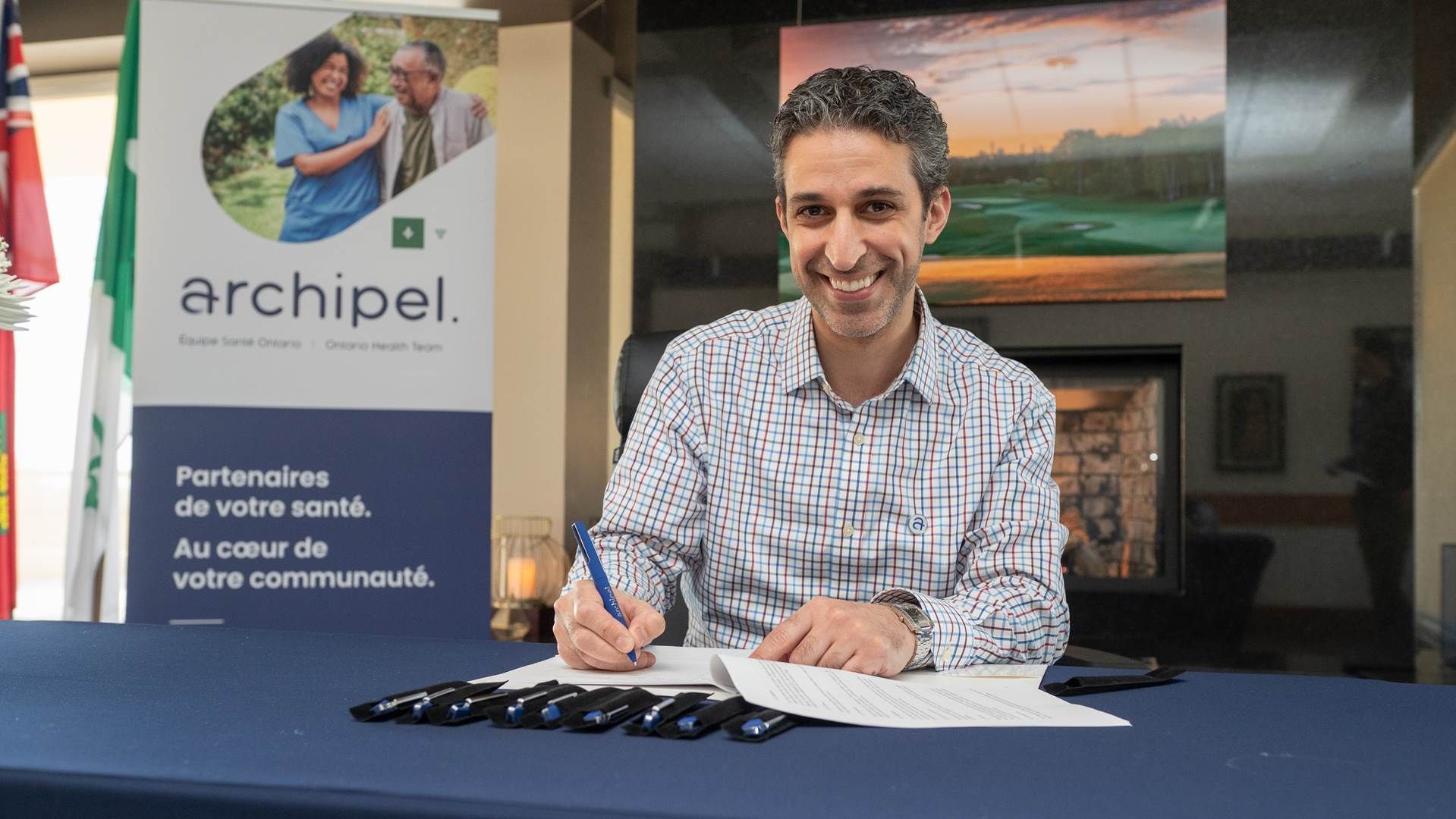 Un homme signe un document devant un panneau sur lequel est écrit archipel.