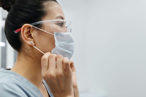 Une femme portant un masque chirurgical et des lunettes de protection.