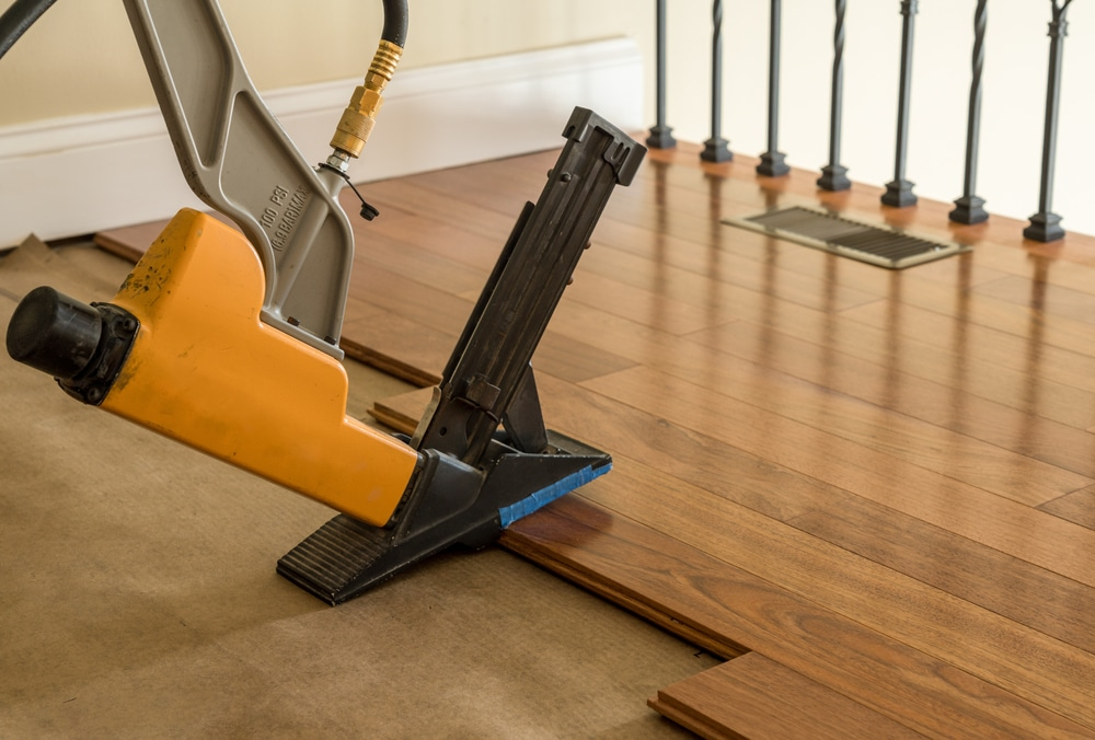 Orange and black pneumatic flooring nailer installing hardwood flooring in a room.