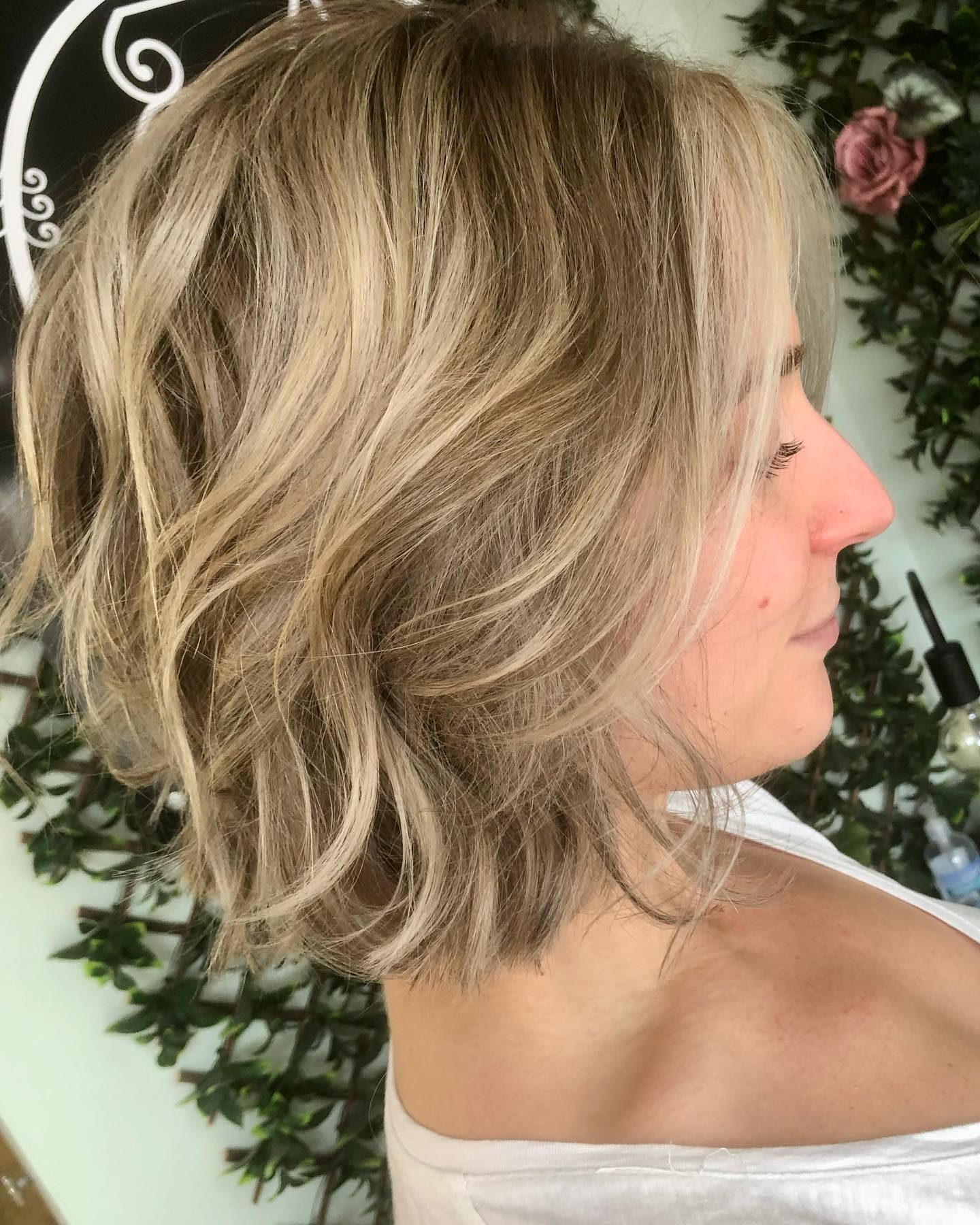 A side profile of a person with chin-length, wavy blonde hair featuring highlights in a salon setting.