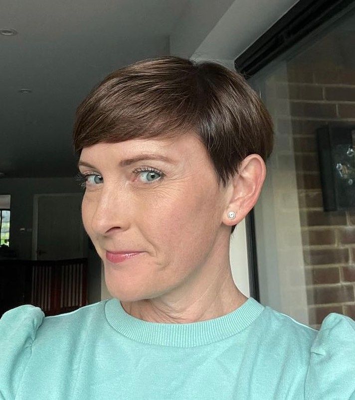 A person with short brown hair and blue eyes wears a light blue sweater, looking toward the camera with a subtle smile.