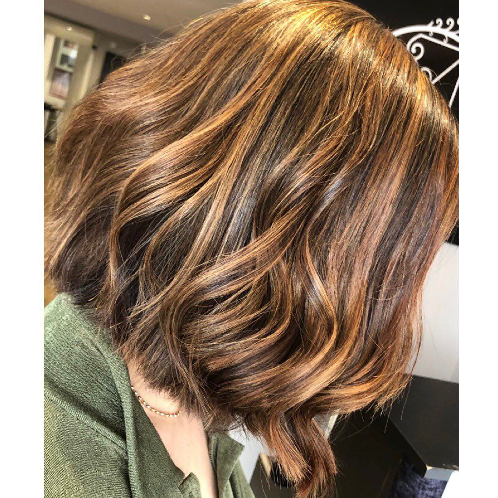 Shoulder-length, wavy brown hair with golden highlights, viewed from the side in a hair salon setting.