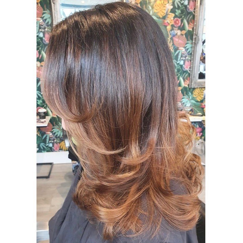 A side profile of medium-length brown hair with soft, layered curls transitioning to a lighter auburn tone at the ends.