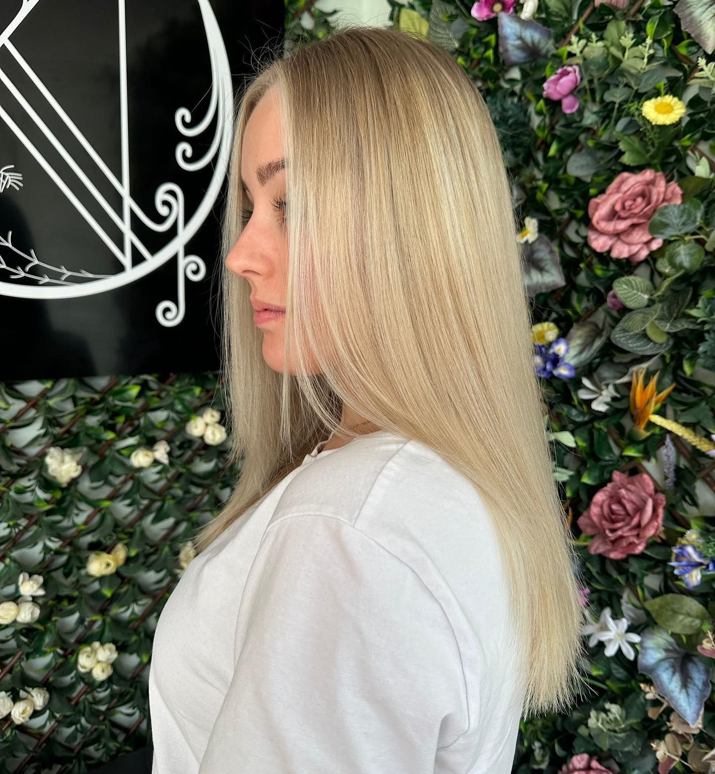 Profile view of a person with long, straight blonde hair standing in front of a floral wall.