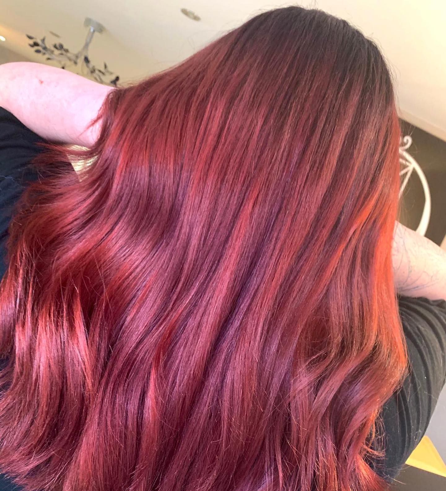 Back view of someone with shoulder-length, vibrant red hair featuring dark roots and lighter, copper-toned ends.