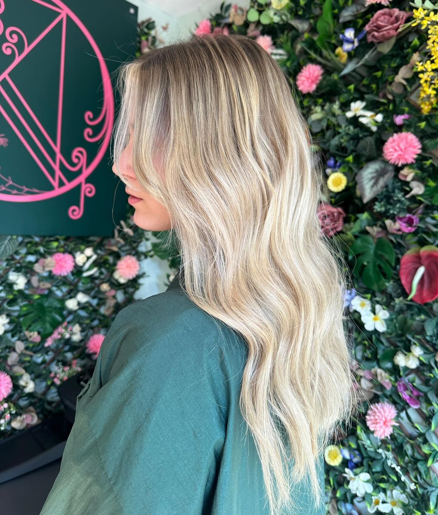 Side profile of long, wavy, highlighted blonde hair against a backdrop of a colorful floral wall.