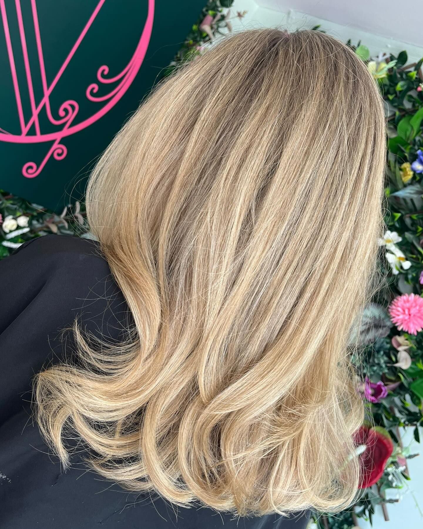 Back view of medium-length, layered blonde hair with highlights, styled in soft waves against a floral background.