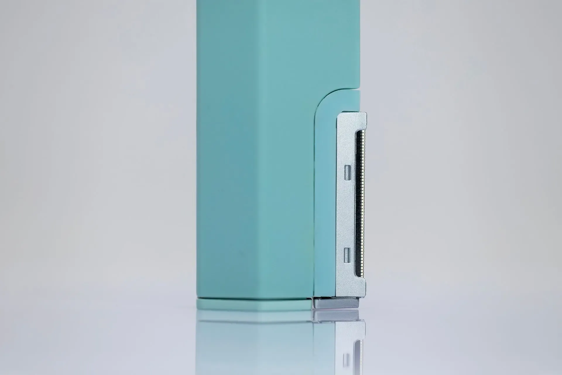 A close-up of a teal, rectangular device with a vertical, metallic strip featuring small, slotted openings on its side.