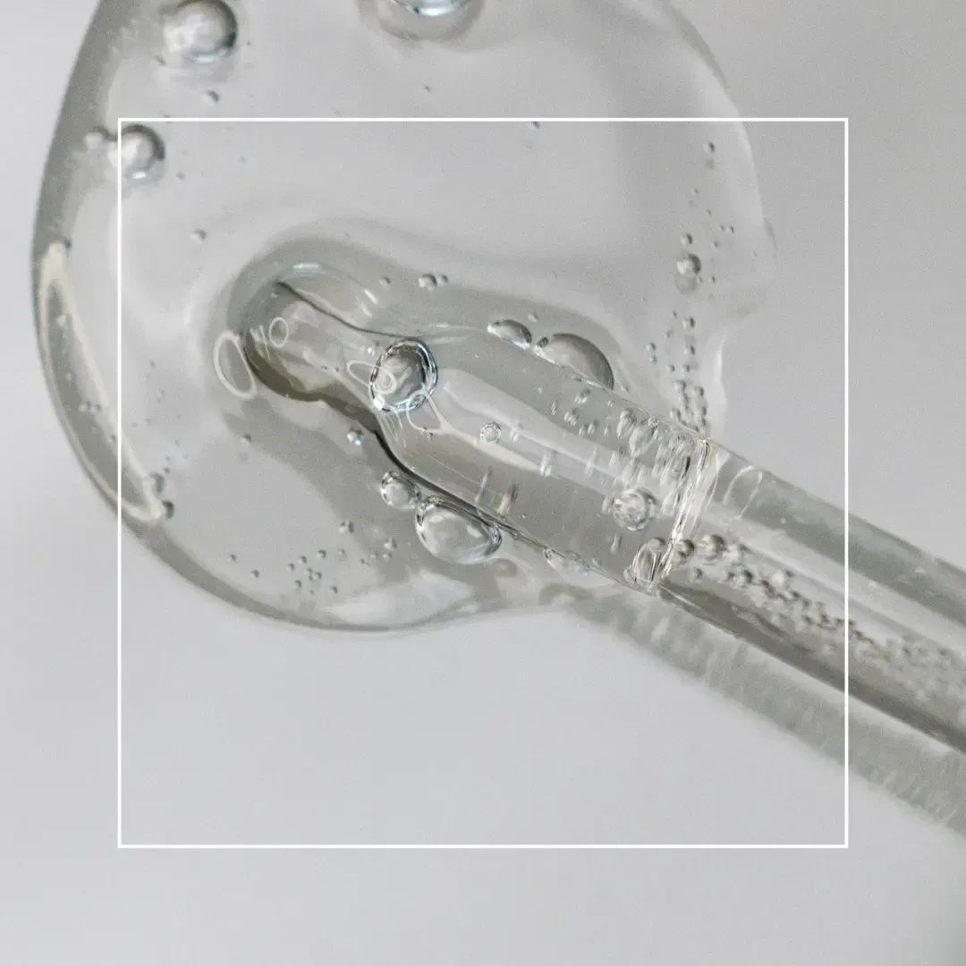 A clear liquid serum dripping from a glass dropper against a clean, light gray background.