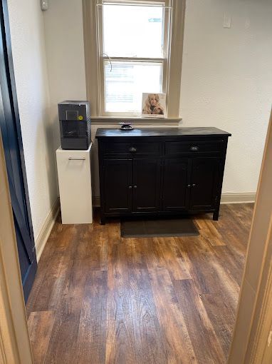 A room with hardwood floors , a black dresser , a water cooler and a window.