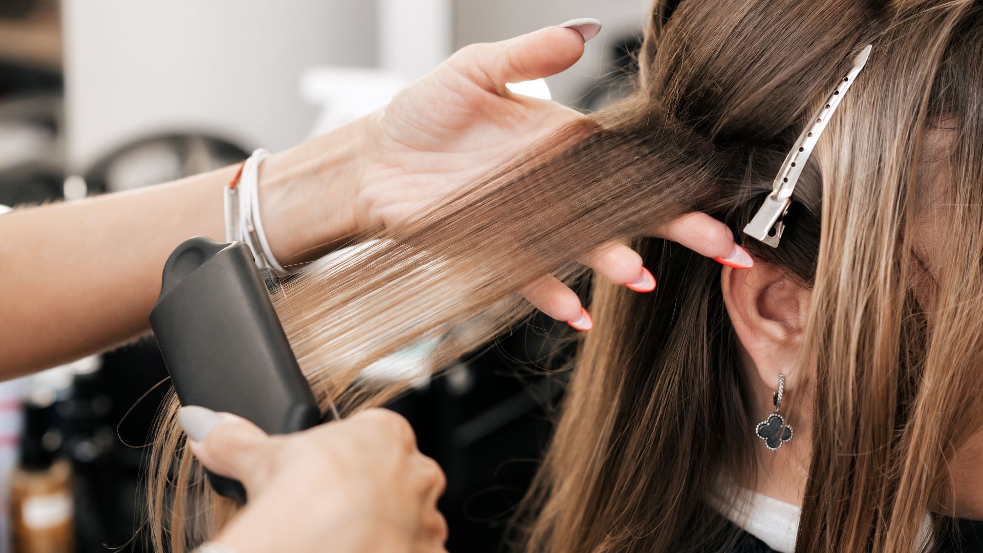 A woman is getting her hair straightened by a hairdresser in a salon.