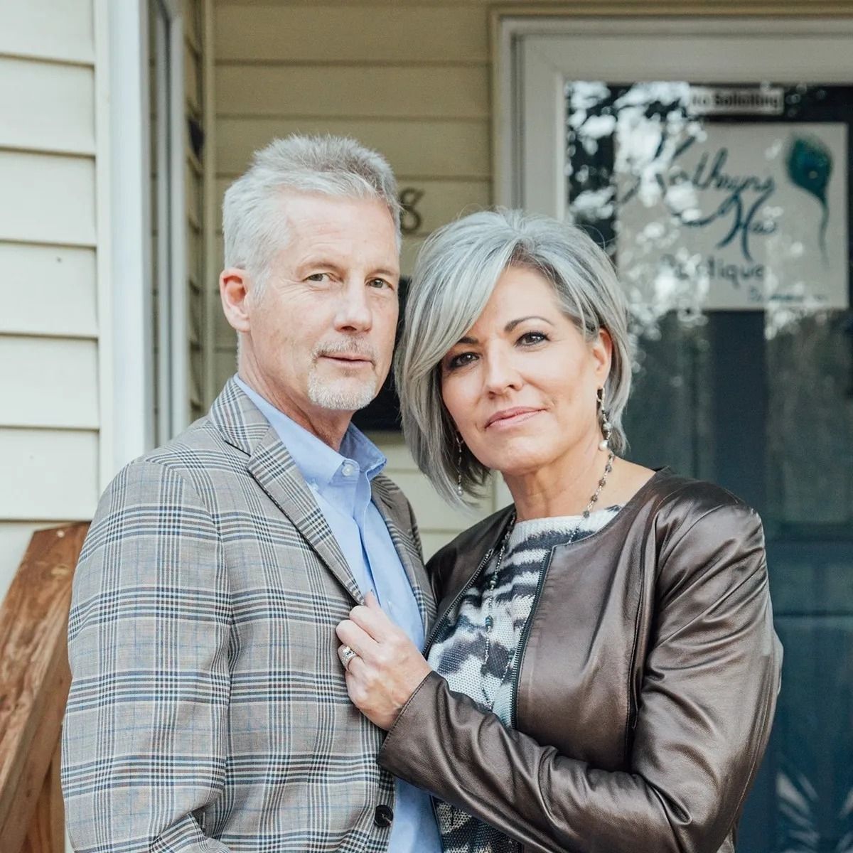 A man and a woman are posing for a picture in front of a house.
