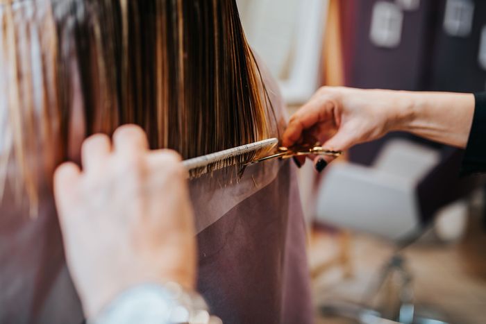 A row of chairs in a hair salon with a woman standing in the background.