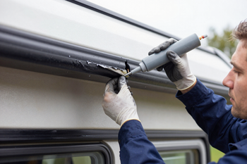 Tecnico che installa una tenda da sole sul tetto di un furgone bianco utilizzando un utensile elettrico.