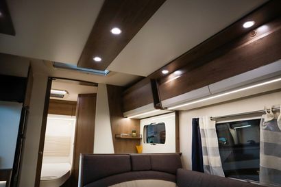 Un camper parcheggiato in riva a un lago sotto un cielo azzurro brillante con nuvole, sedie e un frigo portatile all'esterno.